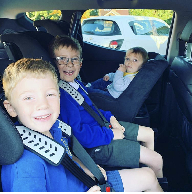 Superclub + Minimac 3 children sat in blue in the back of a car in a Multimac , one baby sat backwards while her two brothers are forward facing in the 5 point harness